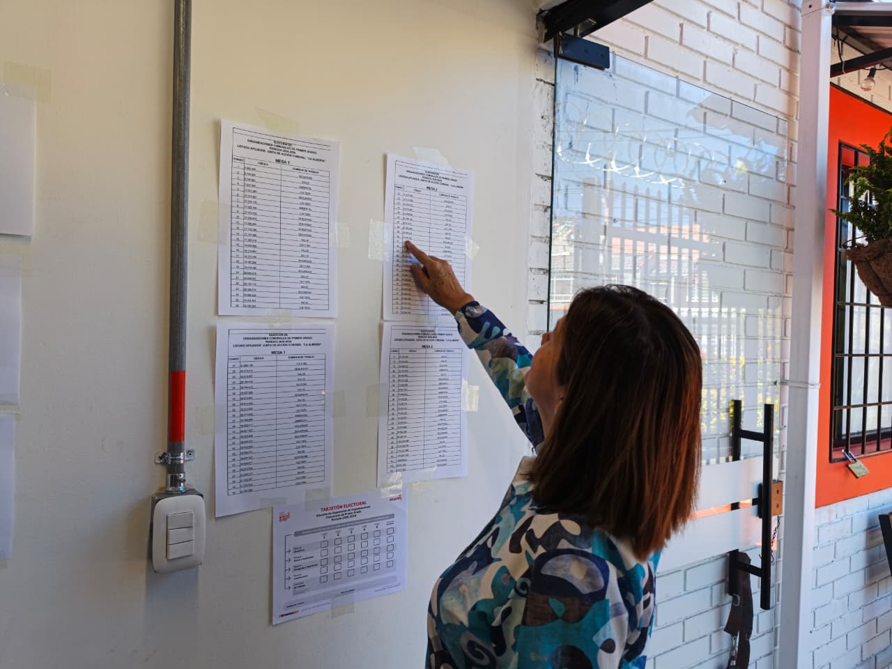 Una ciudadana consulta los listados de censo electoral fijados en la pared de un puesto de votación durante las elecciones de Juntas de Acción Comunal 2026 en Bogotá.