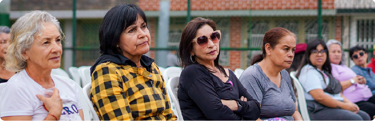 Fotografía de una jornada comunitaria liderada por la Gerencia de Mujer y Género del Instituto Distrital de la Participación y Acción Comunal (IDPAC). En la imagen se observa un grupo de mujeres asistentes escuchando atentamente una actividad de participación ciudadana al aire libre, en un espacio orientado al diálogo, el fortalecimiento del liderazgo y la promoción de los derechos de las mujeres en Bogotá.