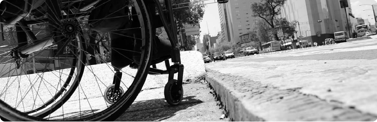 Persona usuaria de silla de ruedas junto a un andén en un entorno urbano de Bogotá.