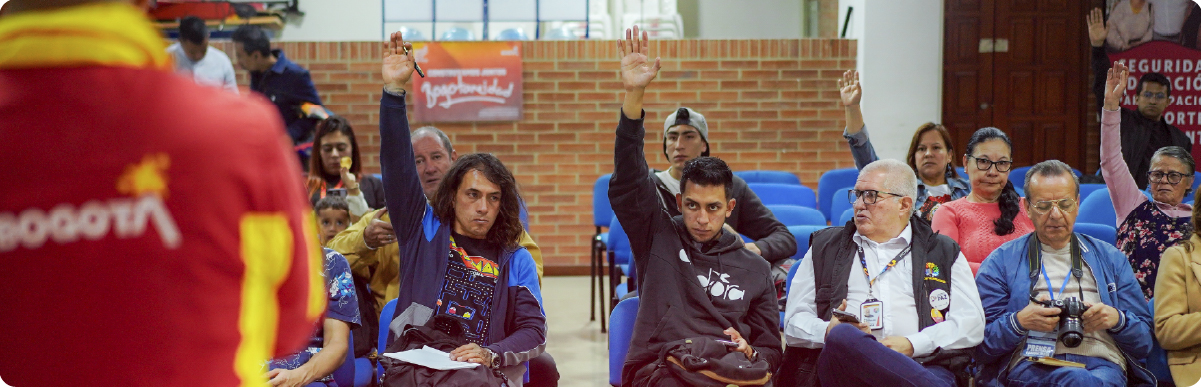 Fotografía de una jornada liderada por la Subdirección de Fortalecimiento a Organizaciones Sociales del Instituto Distrital de la Participación y Acción Comunal (IDPAC). En la imagen se observa a varias personas asistentes participando activamente en una reunión, levantando la mano para intervenir o votar durante un espacio de diálogo y fortalecimiento de las organizaciones sociales en Bogotá.