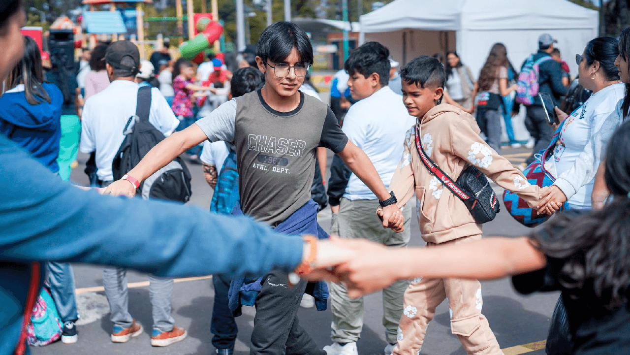 Niñas, niños y adolescentes participan en una actividad lúdica tomados de las manos durante el Festival INN Comunalitos en Bogotá, fomentando el trabajo en equipo y la integración comunitaria.