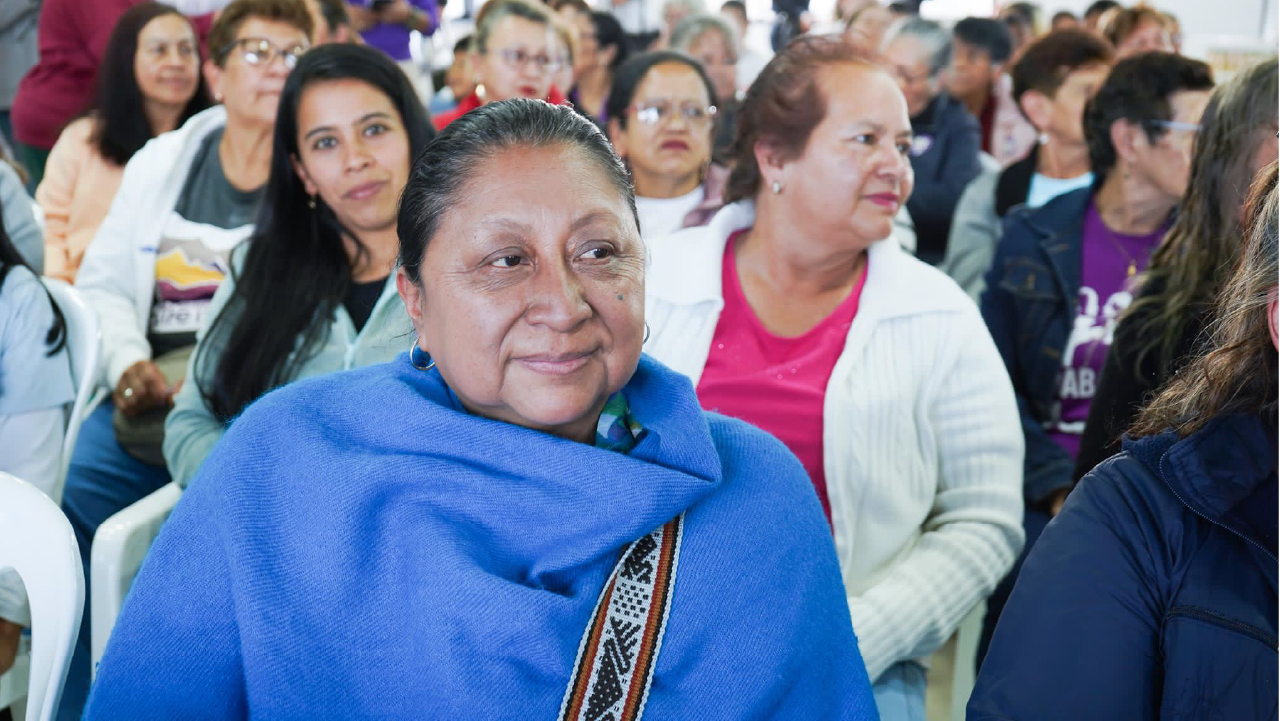 Mujer adulta envuelta en un chal azul participa en un encuentro comunitario en Bogotá, rodeada de otras asistentes