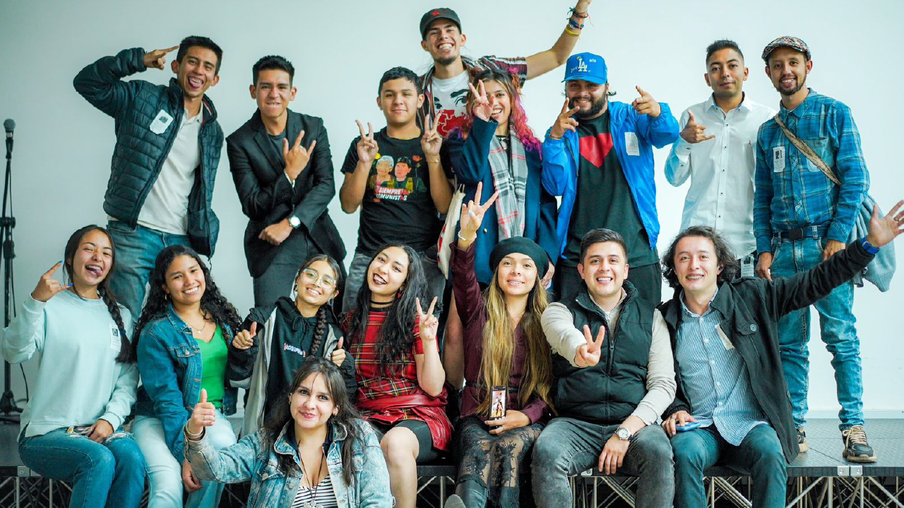 Grupo diverso de jóvenes participantes posando juntos y celebrando con gestos de victoria durante un encuentro de participación juvenil en Bogotá