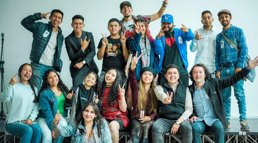 Grupo diverso de jóvenes participantes posando juntos y celebrando con gestos de victoria durante un encuentro de participación juvenil en Bogotá