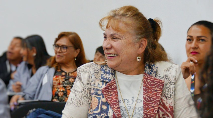 Mujer mayor sonríe durante un encuentro institucional con otras personas participantes, en un espacio de diálogo y fortalecimiento de la participación ciudadana en Bogotá.